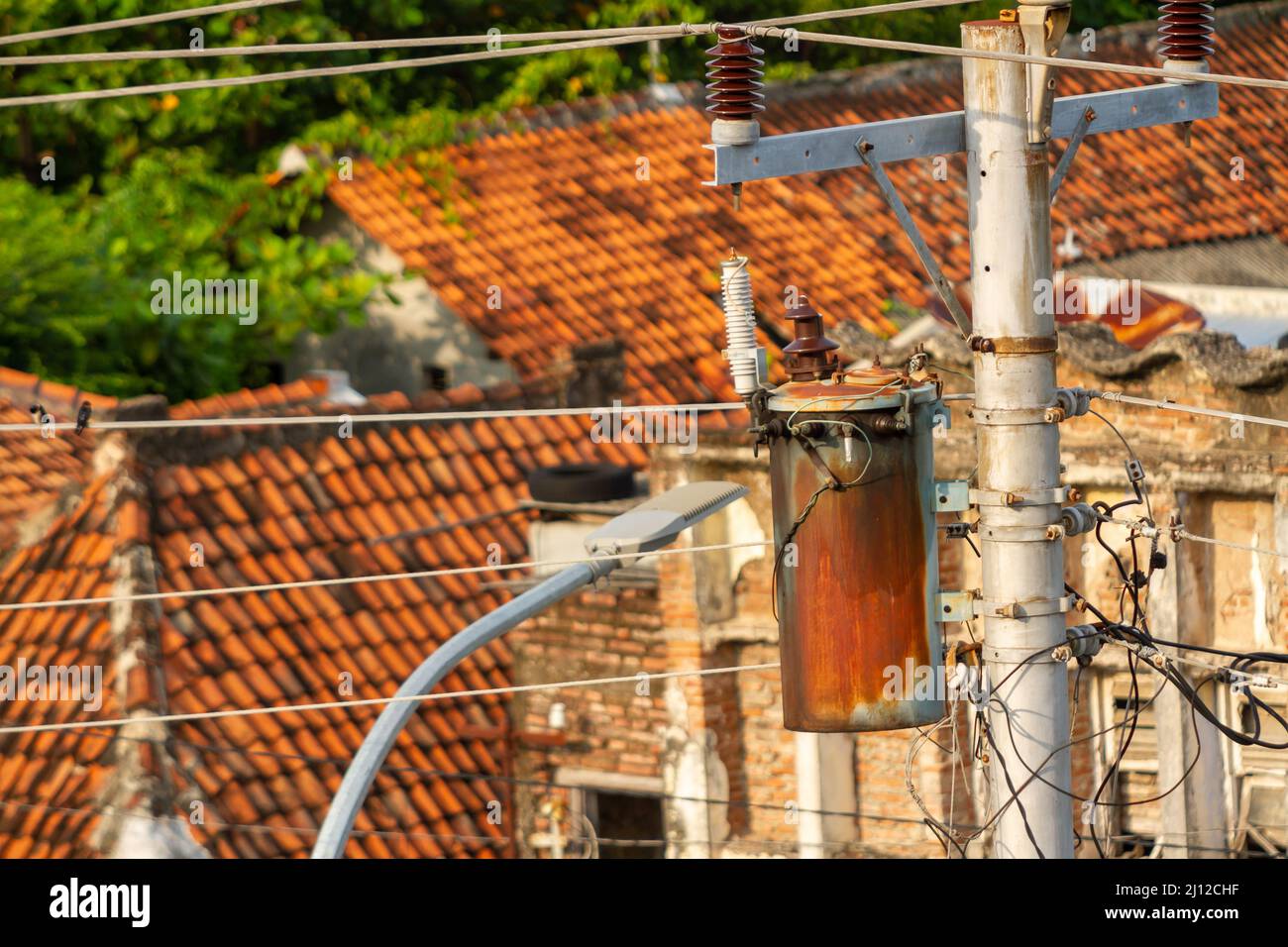 Réseau d'installation électrique avec des poteaux en béton dans les rues côte à côte avec des maisons de personnes en Indonésie, entre les besoins énergétiques et le danger Banque D'Images