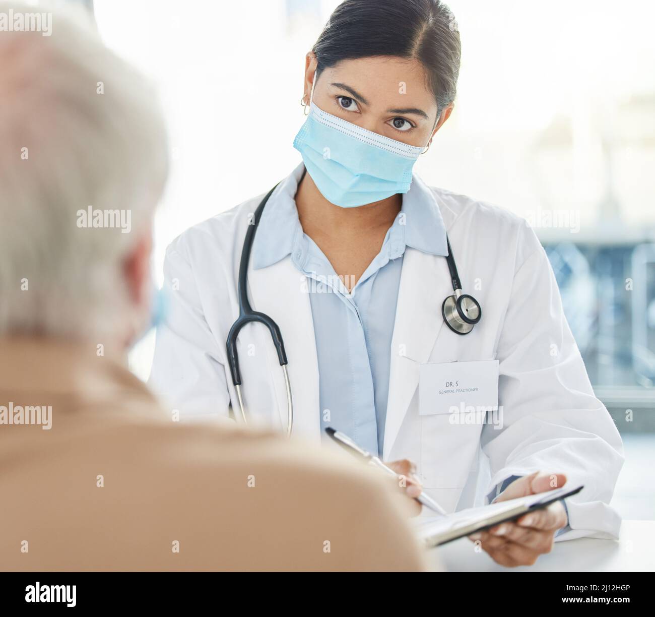 Etes-vous allergique à quoi que ce soit. Prise de vue d'un médecin portant un masque facial et assis avec sa patiente senior pendant une consultation dans sa clinique. Banque D'Images