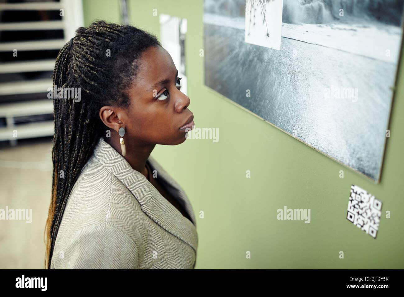 Gros plan moyen grand angle de la jeune femme noire pensive avec des tresses afro hairstyle visite exposition contemporaine regardant la photo sur le mur Banque D'Images