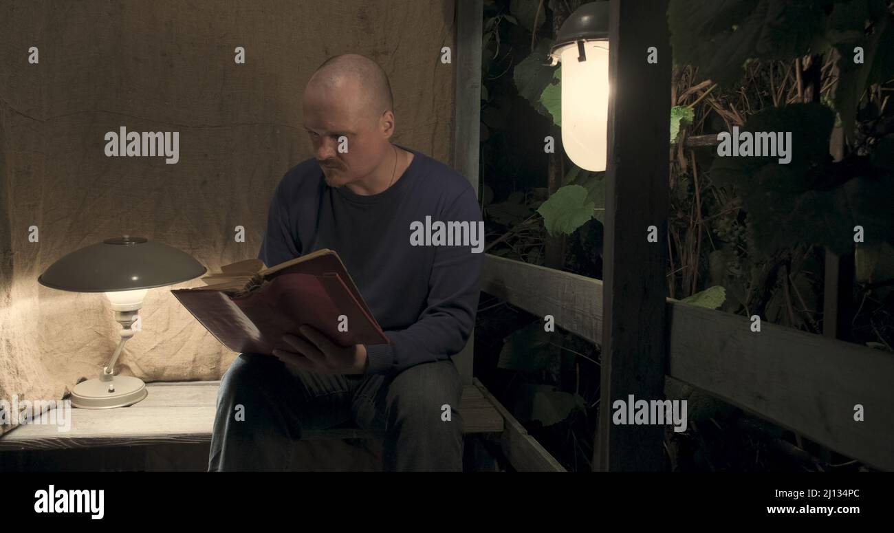 L'homme est assis sur un vieux porche du village. Il récupère un vieux livre Banque D'Images