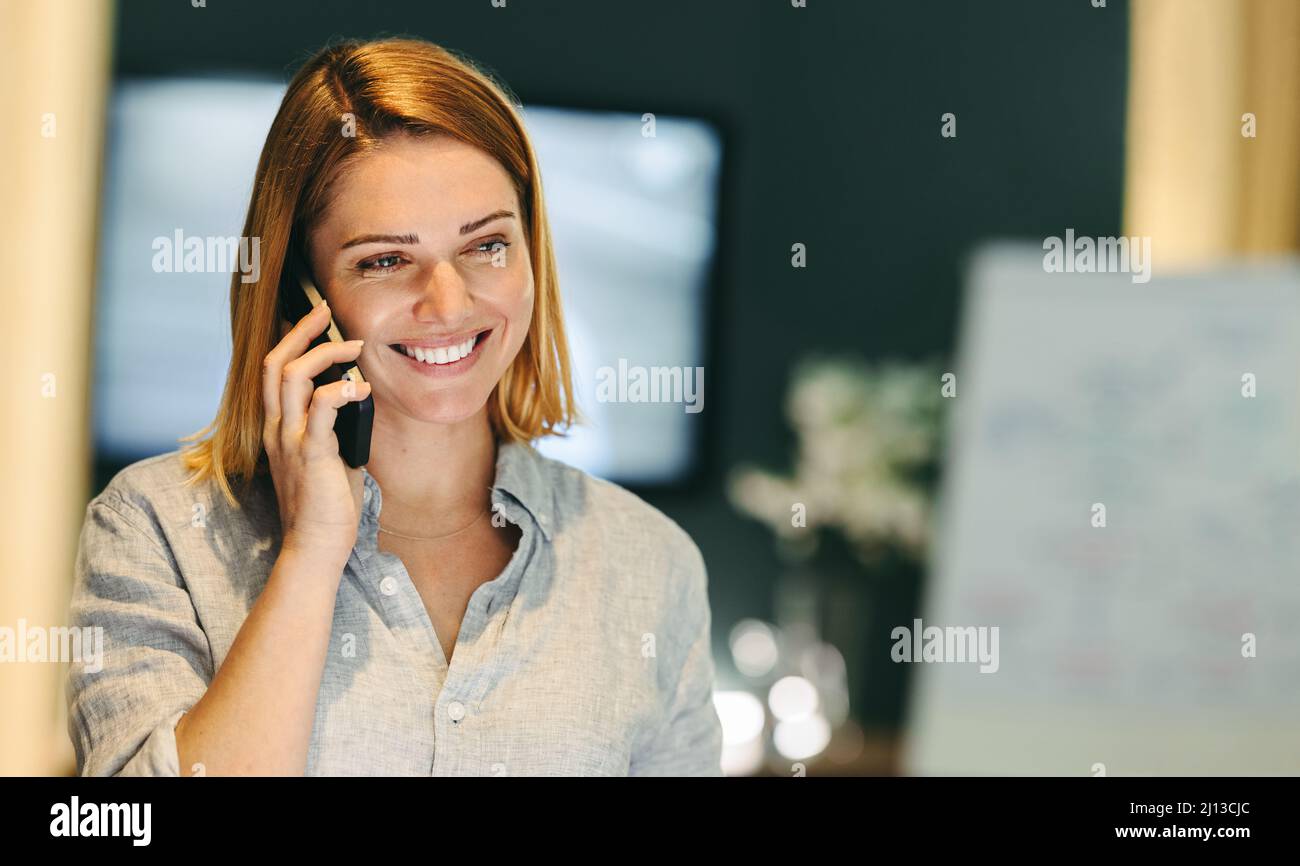 Une jeune femme d'affaires gaie souriant en parlant au téléphone. Femme d'affaires réussie communiquant avec ses associés d'affaires dans un Banque D'Images