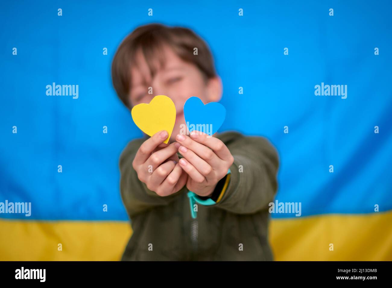 Mains de garçon tenant des coeurs en papier jaune-bleu sur fond de drapeau ukrainien. Les enfants soutiennent l'Ukraine, arrêtent la guerre, restent avec le hashtag de l'Ukraine Banque D'Images
