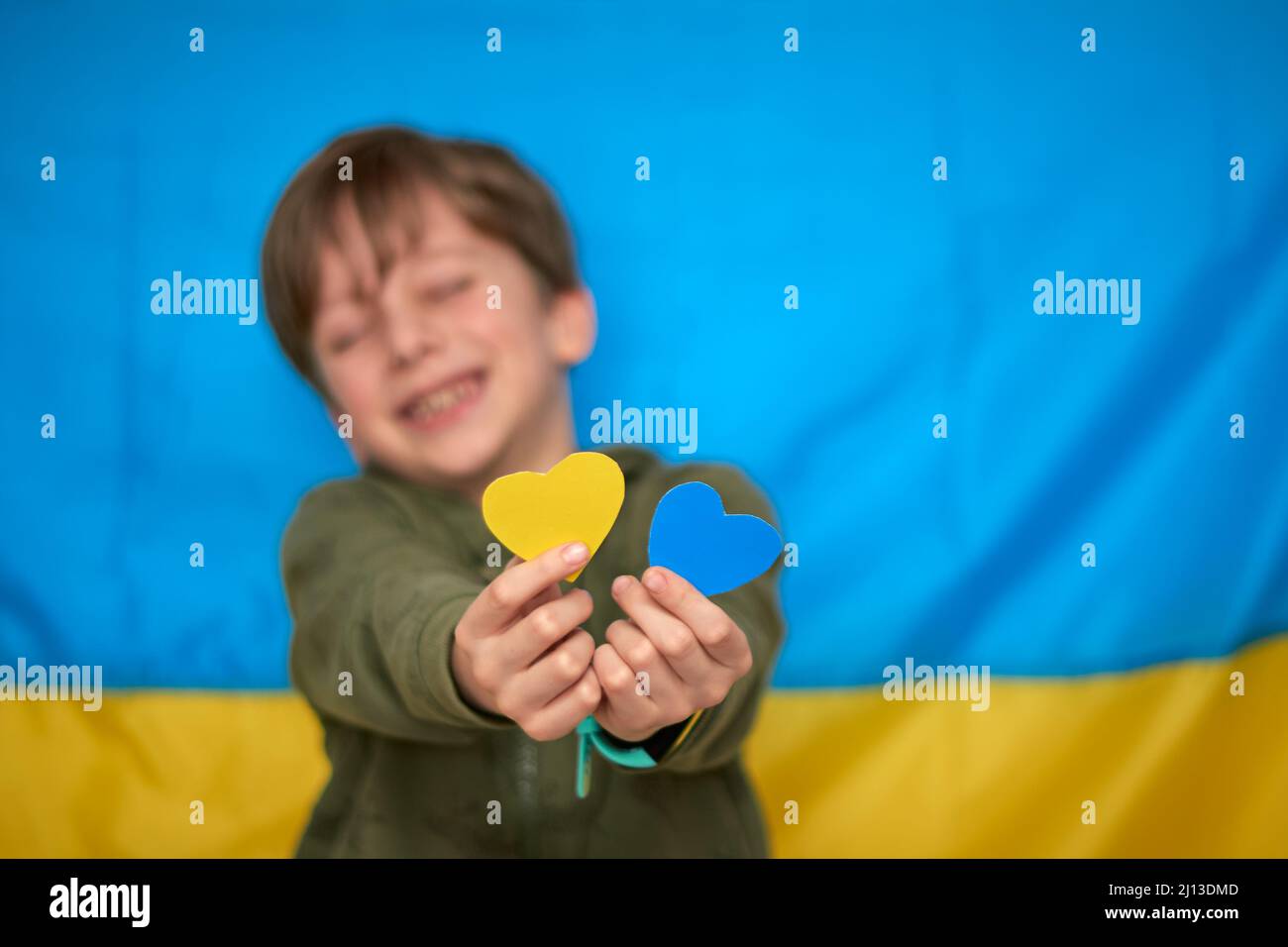 Mains de garçon tenant des coeurs en papier jaune-bleu sur fond de drapeau ukrainien. Les enfants soutiennent l'Ukraine, arrêtent la guerre, restent avec le hashtag de l'Ukraine Banque D'Images