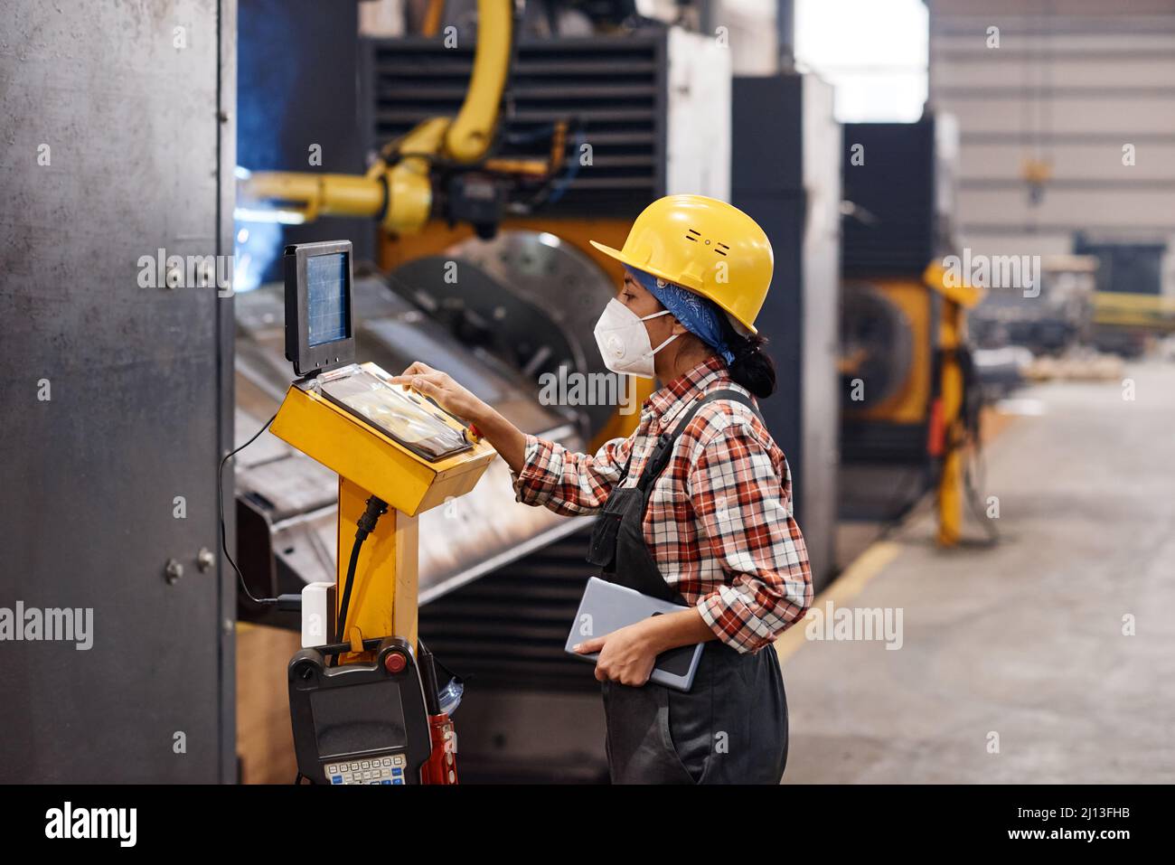 Vue latérale de la jeune femme ingénieur en respirateur, casque et combinaison, montrant le document contenant les informations techniques en usine Banque D'Images