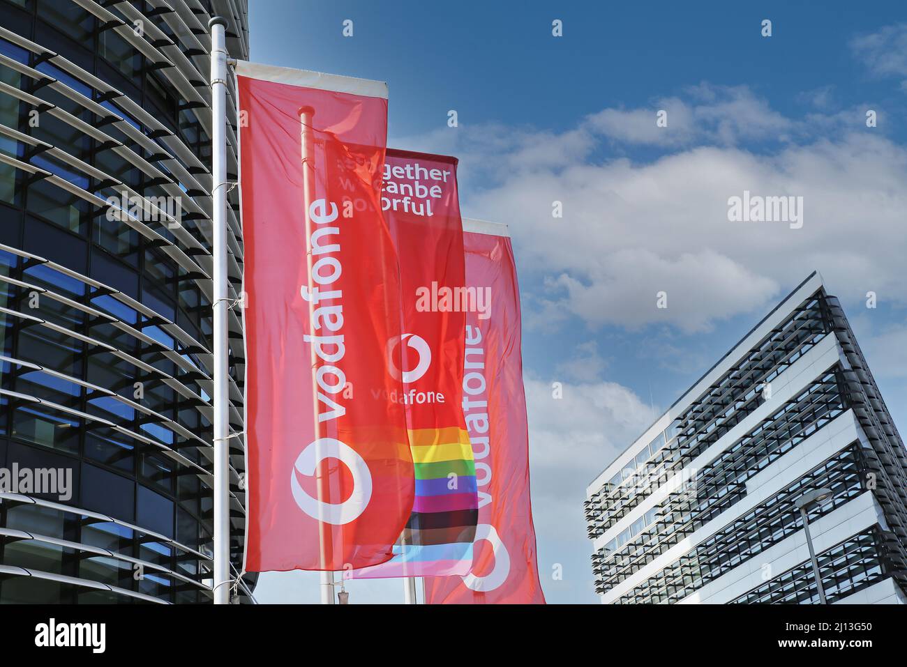 Düsseldorf (campus de Vodafone) - Mars 9. 2022: Vue sur les drapeaux rouges à l'entrée du bâtiment administratif futuriste moderne contre le ciel bleu Banque D'Images