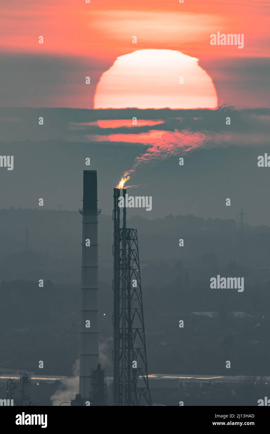 Un panache d'émissions s'écoule de la cheminée de Stanlow au port d'Ellesmere contre un coucher de soleil brumeux, alors que les prix du carburant continuent d'augmenter. Royaume-Uni, mars 2022 Banque D'Images