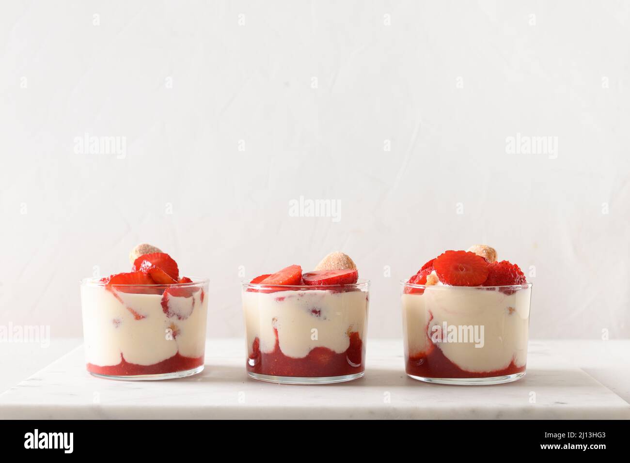 Trois portions de dessert de trifle en pots de verre avec biscuit savoyardi, fromage mascarpone décoré de fraises sur fond blanc. Banque D'Images