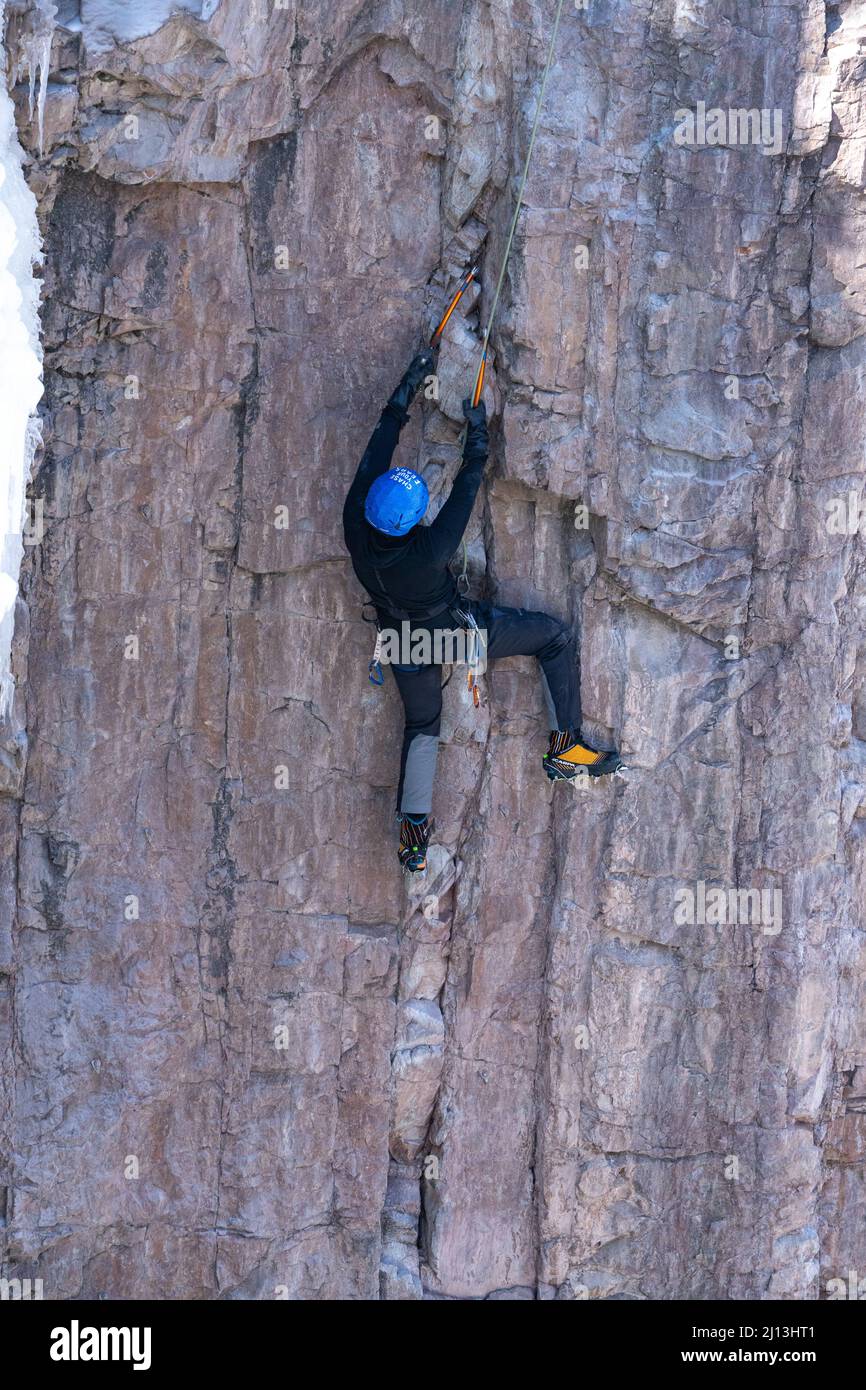 Un grimpeur sportif sur une ascension mixte, utilisant des haches de glace et des crampons pour grimper un mur de roche dans le parc de glace d'Ouray dans le Colorado. La section de roche est entourée Banque D'Images