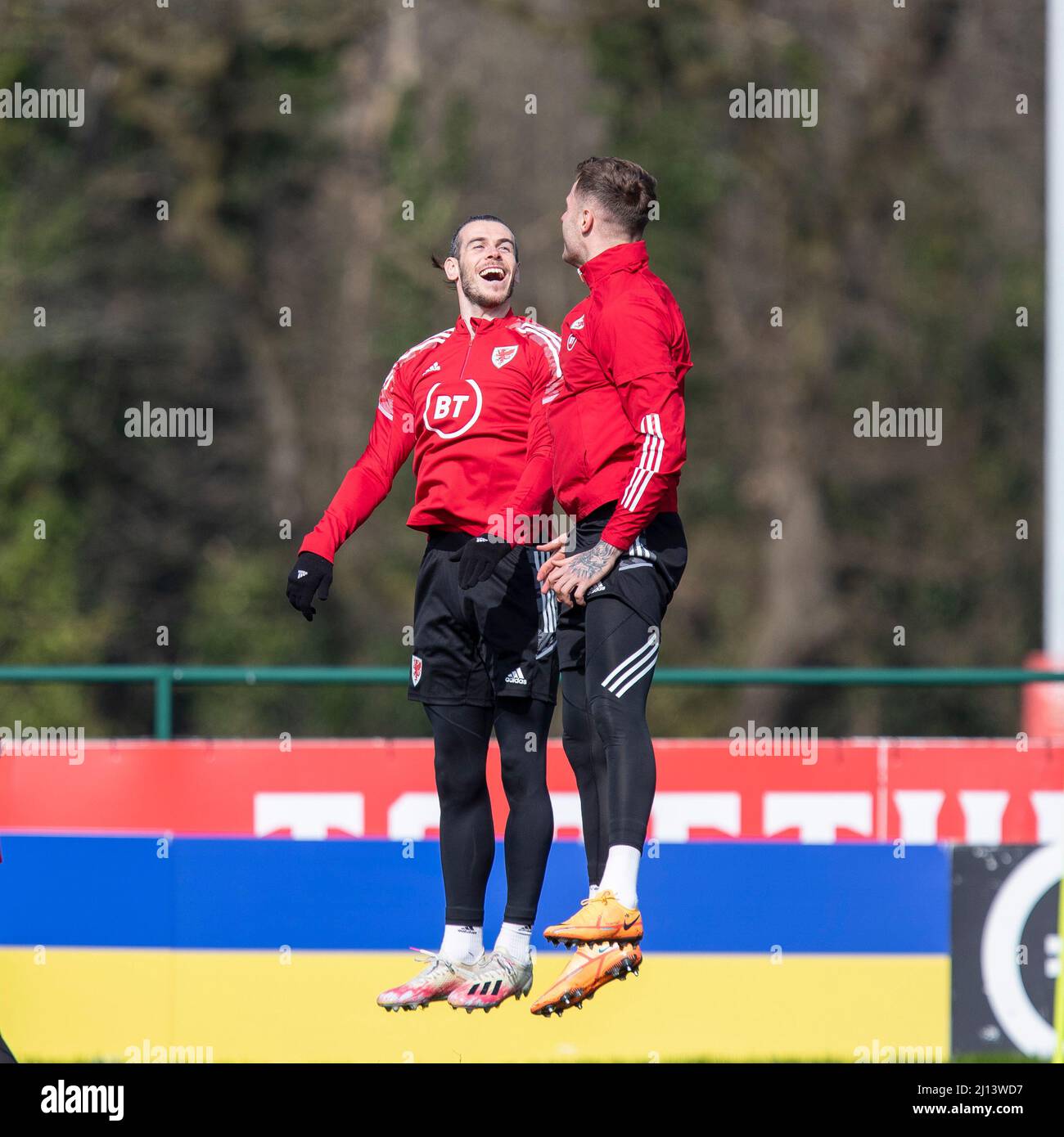 Hensol, pays de Galles, Royaume-Uni. 22nd mars 2022. Gareth Bale bondit avec Joe Rodon devant une palissade montrant les couleurs du drapeau ukrainien pendant l'entraînement de l'équipe nationale de football du pays de Galles à Vale Resort avant le match de demi-finale de la coupe du monde 2022 du côté contre l'Autriche. Crédit : Mark Hawkins/Alay Live News Banque D'Images