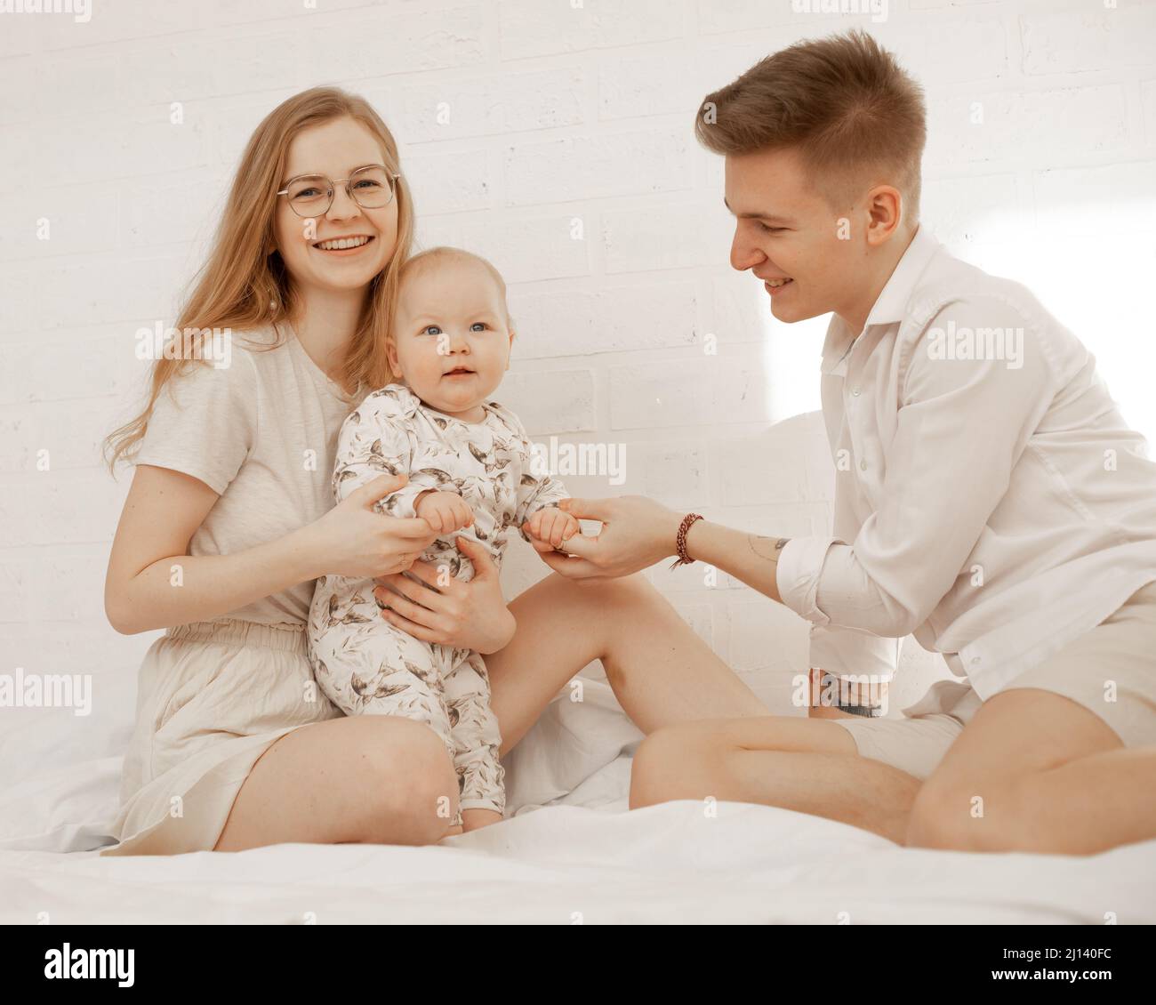 Joyeux famille de femme, d'homme et de bébé couché dans un couvre-lit blanc. Un mode de vie sain et actif. Massage des mains Banque D'Images