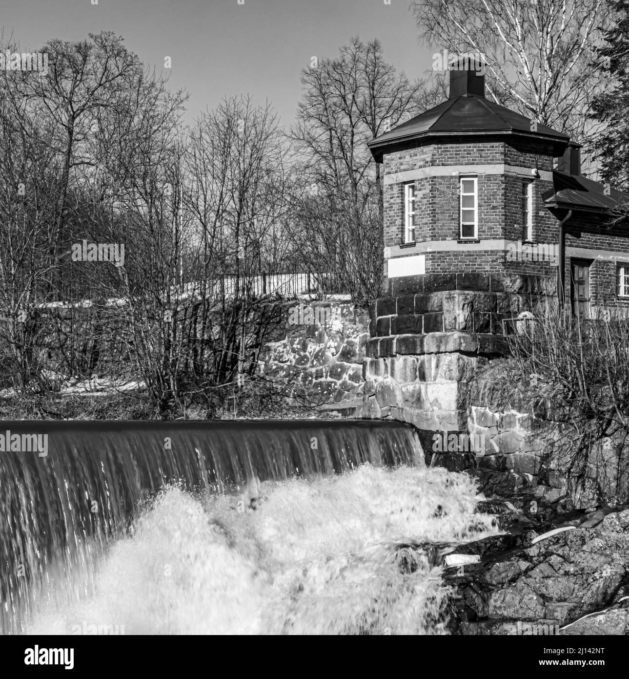Un bâtiment octogonal en briques par les rapides de Vanhankaupunginkoski à Vanhakaupunki, Helsinki, Finlande. Niveaux de gris. Banque D'Images