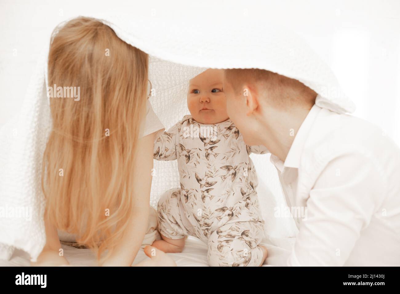 Joyeux joyeux famille satisfaite de femme, d'homme et de bébé couché dans un couvre-lit blanc. Maison de construction de la serviette de recouvrement. Banque D'Images