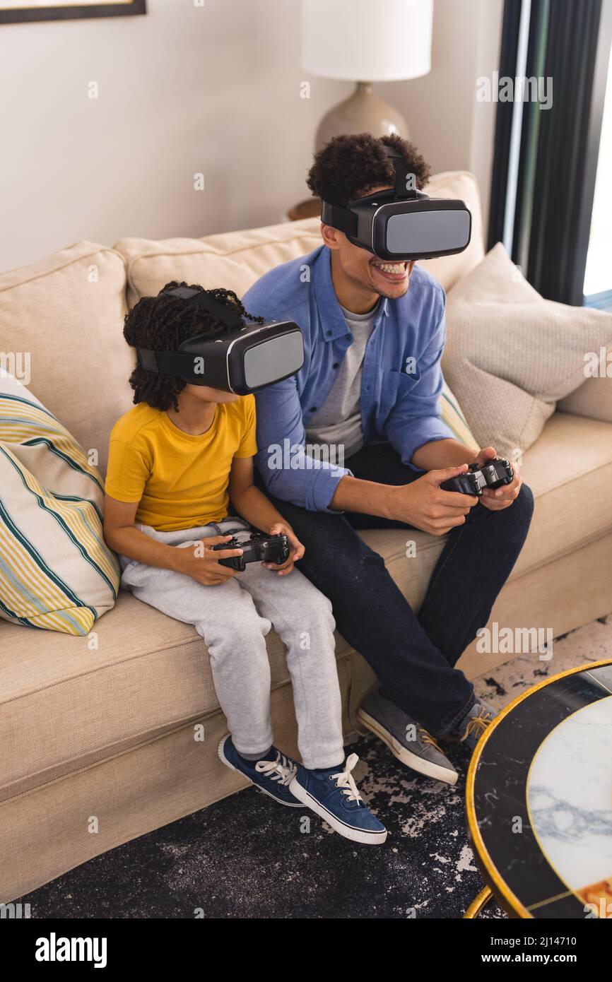 Père et fils hispaniques portant un casque vr jouant à des jeux vidéo dans le salon à la maison Banque D'Images