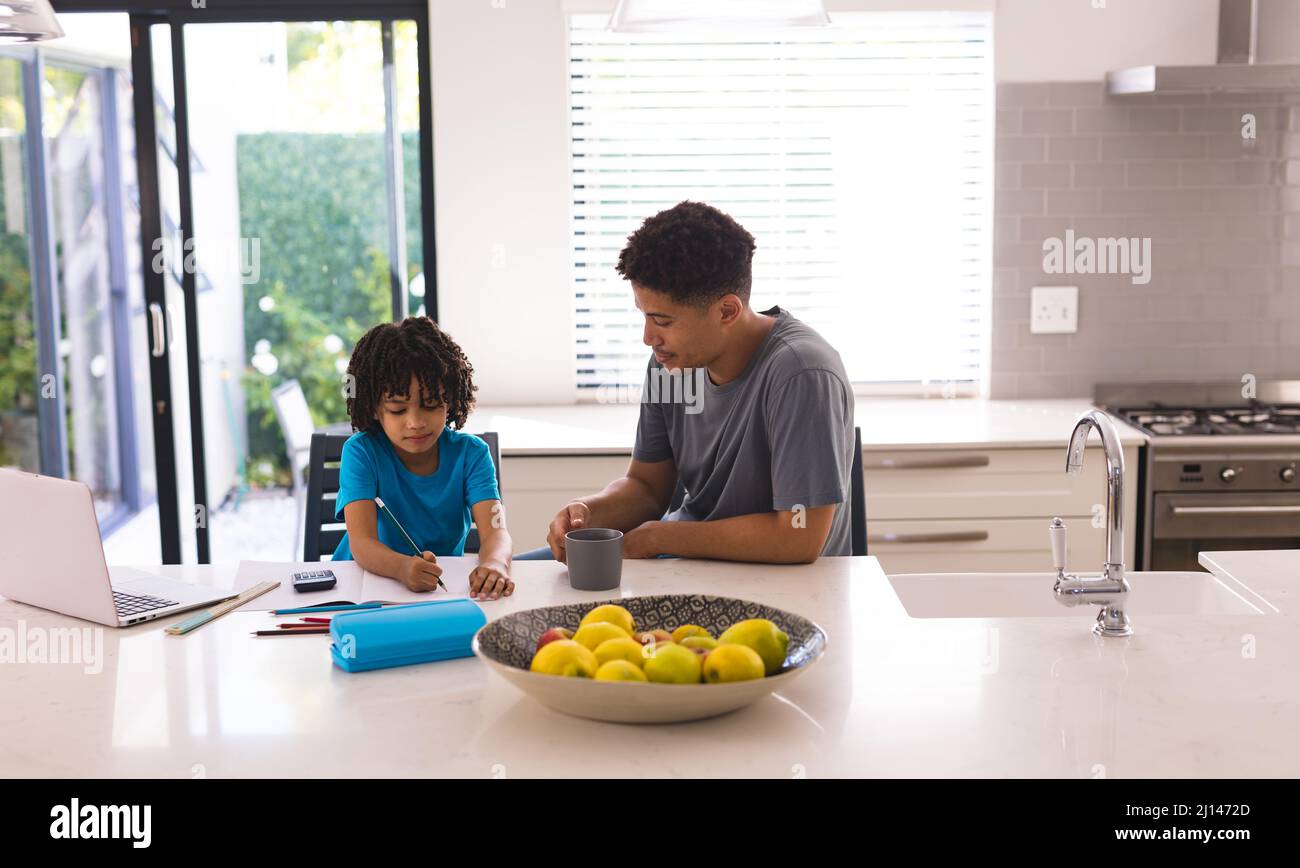 Homme hispanique assis par son fils faisant ses devoirs à Kitchen Island Banque D'Images