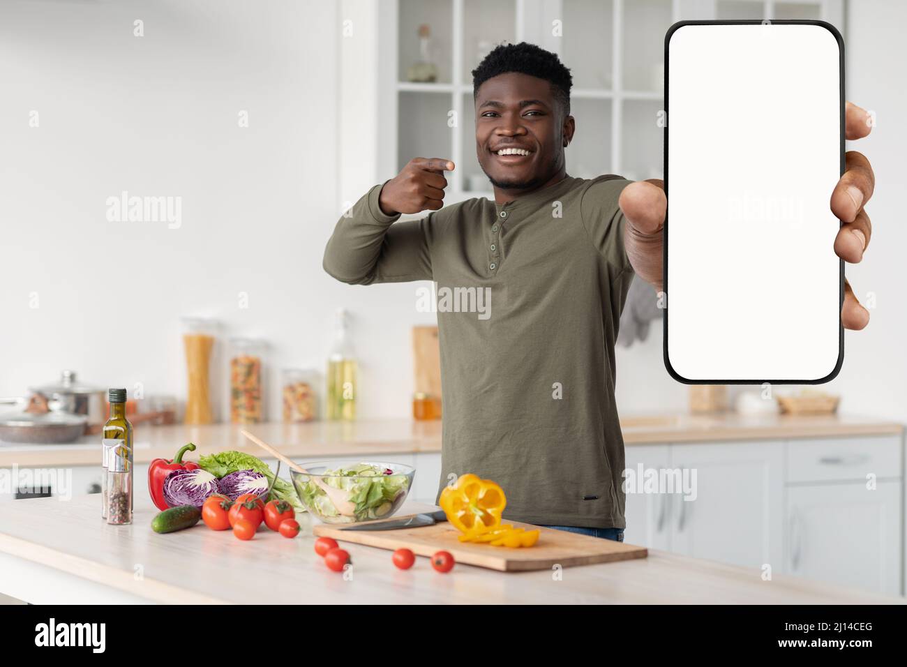 Excellente application Black Guy debout dans la cuisine et pointant vers Blank smartphone Banque D'Images