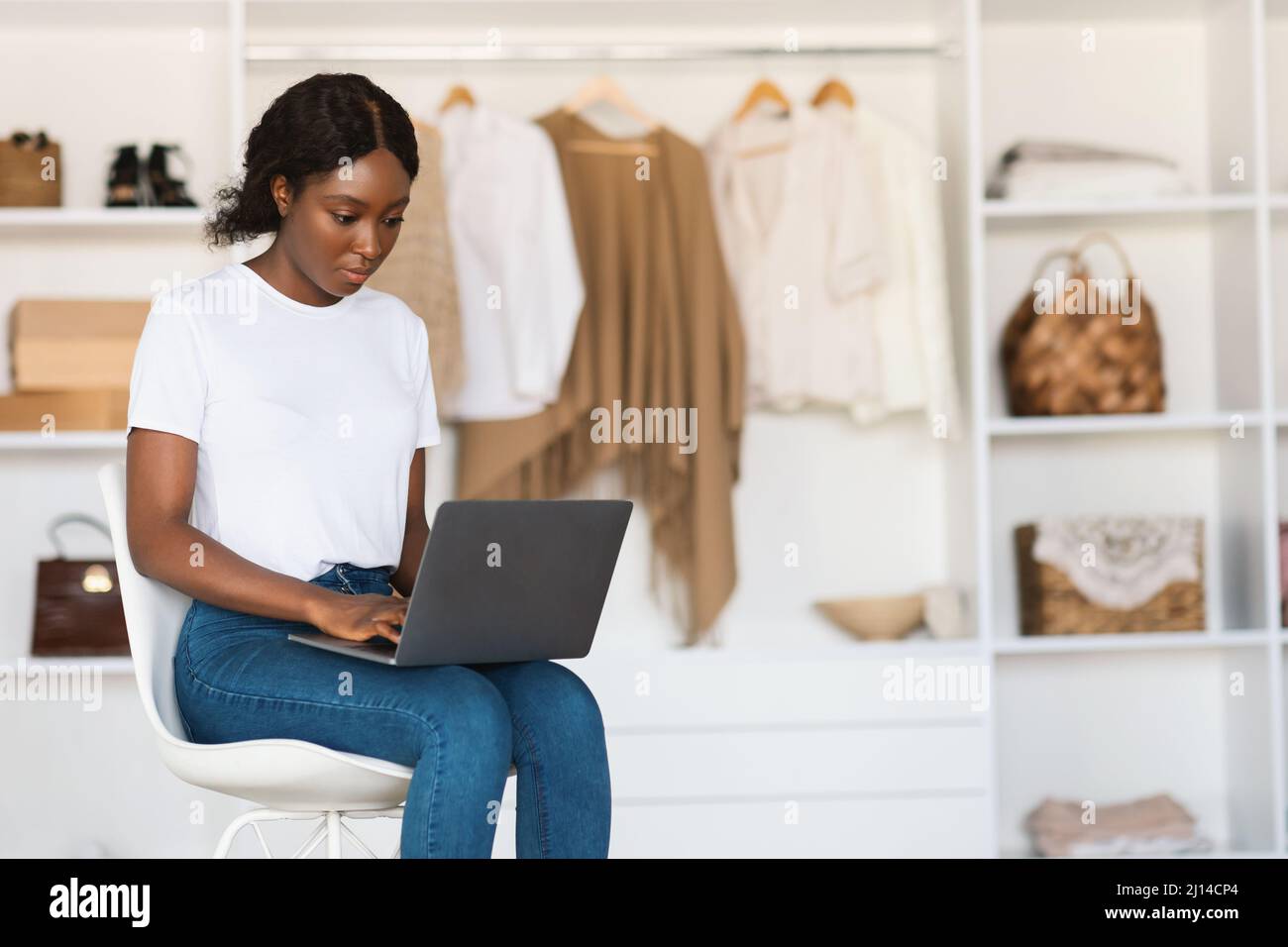 Femme noire sérieuse utilisant le dactylographie d'ordinateur portable assis dans la salle de garde-robe Banque D'Images