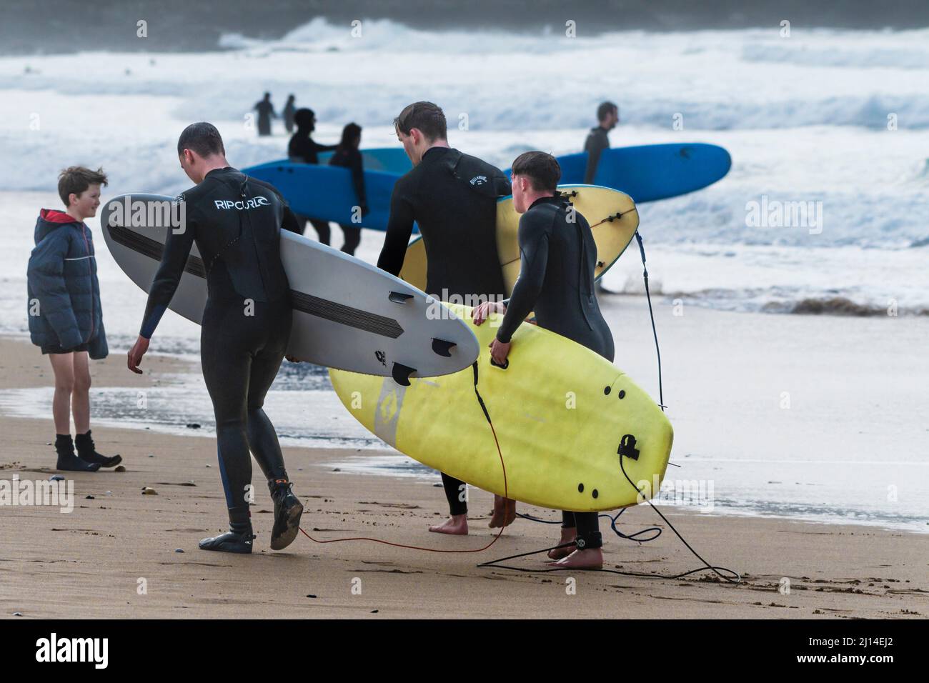 Surfeurs fatigués transportant leurs planches de surf le long du rivage à Fistral Beach à Newquay, en Cornouailles, au Royaume-Uni. Banque D'Images