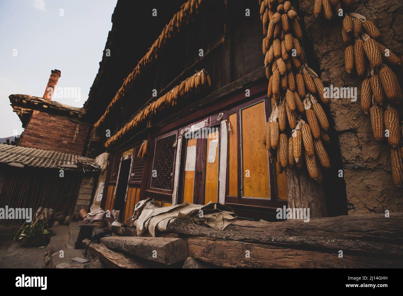 Les anciens extérieurs de maisons traditionnelles chinoises de terre ou de maisons de rafle, corncobs pendent sur les piliers en bois et sur le linteau. Yunnan, Chine. Banque D'Images