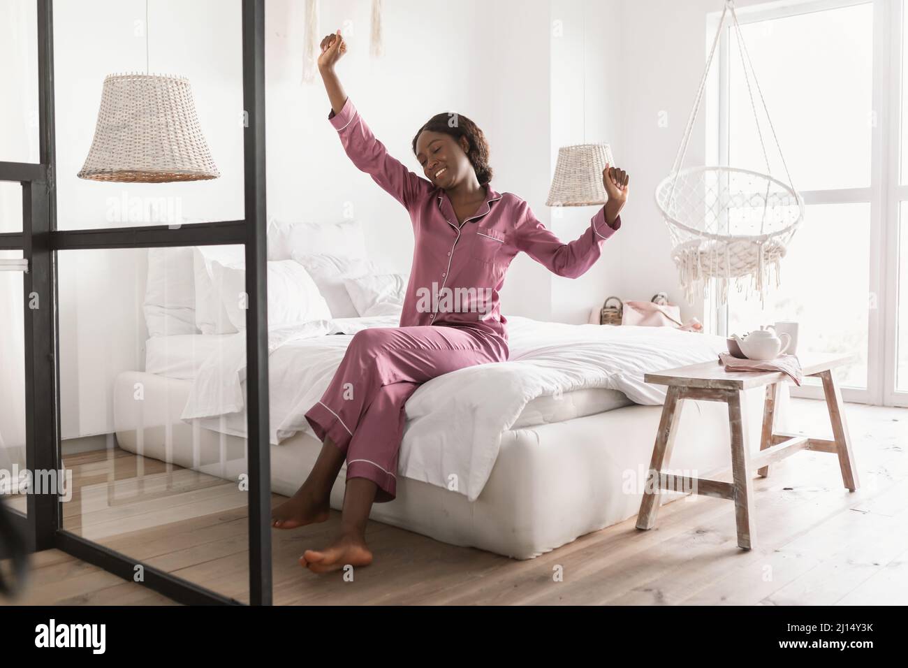 Welldormi Black Lady Stretching Arms portant un pyjama assis dans la chambre Banque D'Images