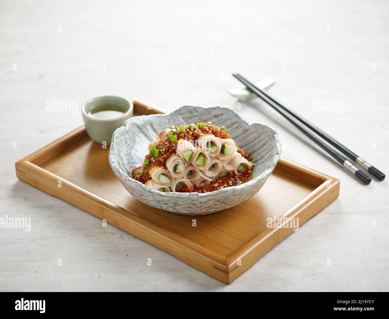 Poitrine de porc en tranches avec sauce épicée à l'ail et sauce, baguettes sur un plat isolé sur panneau de bois vue latérale sur fond gris Banque D'Images