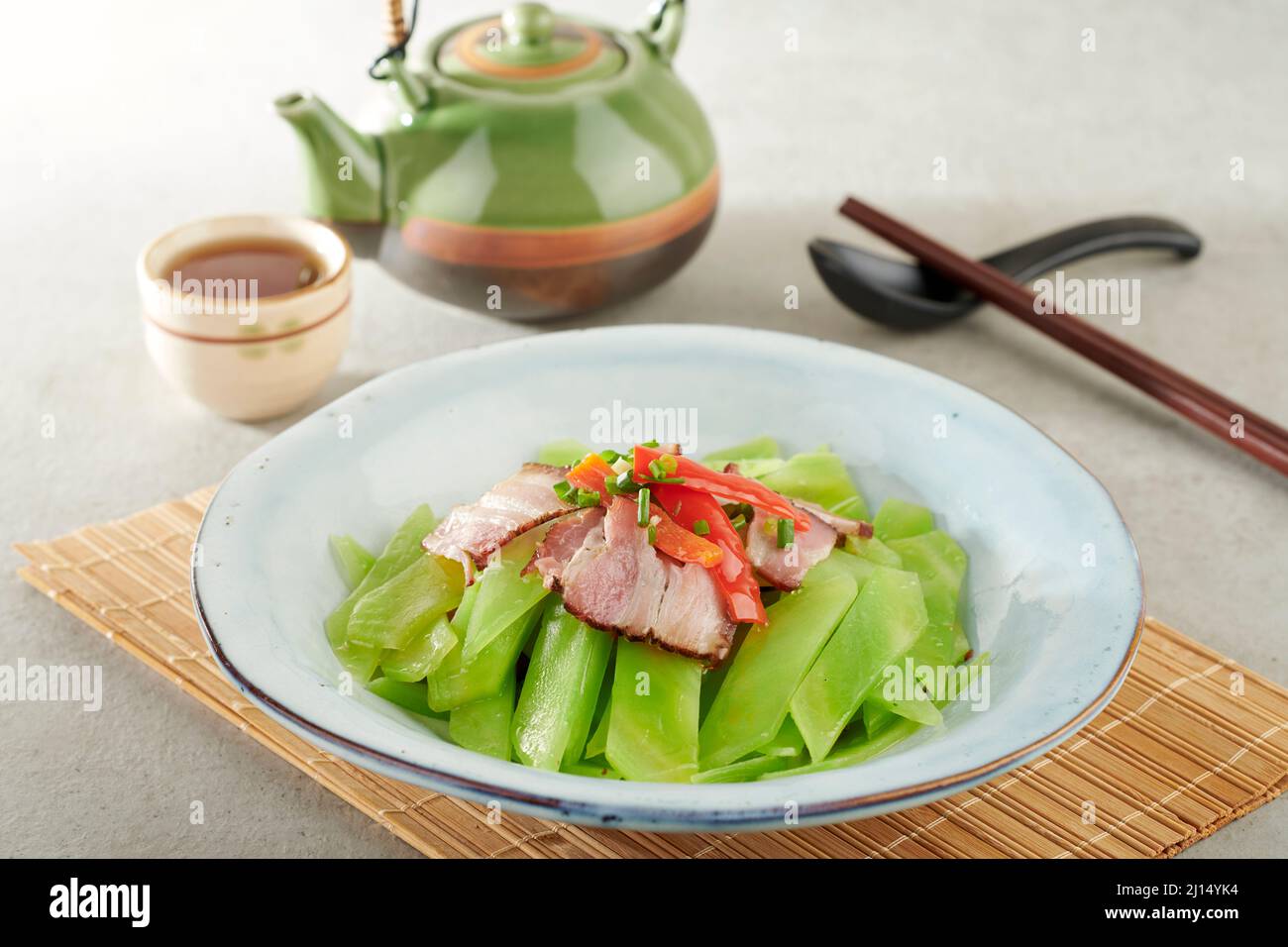 Laitue chinoise sautée avec des morceaux de bacon fumé dans un plat isolé sur un tapis de bois, vue latérale sur fond gris Banque D'Images