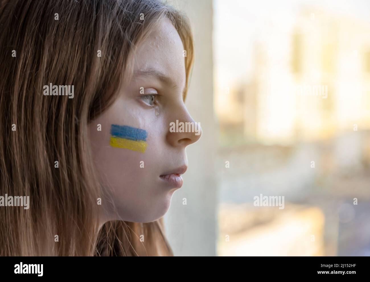 Guerre. Invasion de l'Ukraine par la Russie. Portrait d'un enfant avec des larmes dans les yeux assis sur la table et regardant par la fenêtre. Le bleu et le jaune Banque D'Images