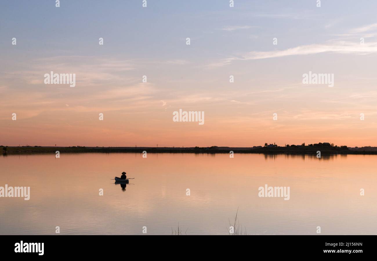 Pêcheur flottant sur le lac STILL au coucher du soleil Banque D'Images