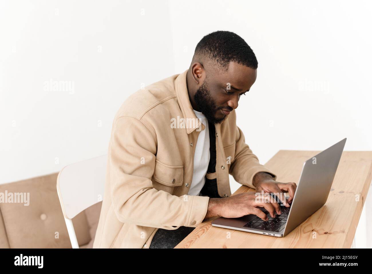 Homme afro-américain concentré travaillant sur un ordinateur portable à domicile. Le programmeur indépendant noir travaille à la table Banque D'Images