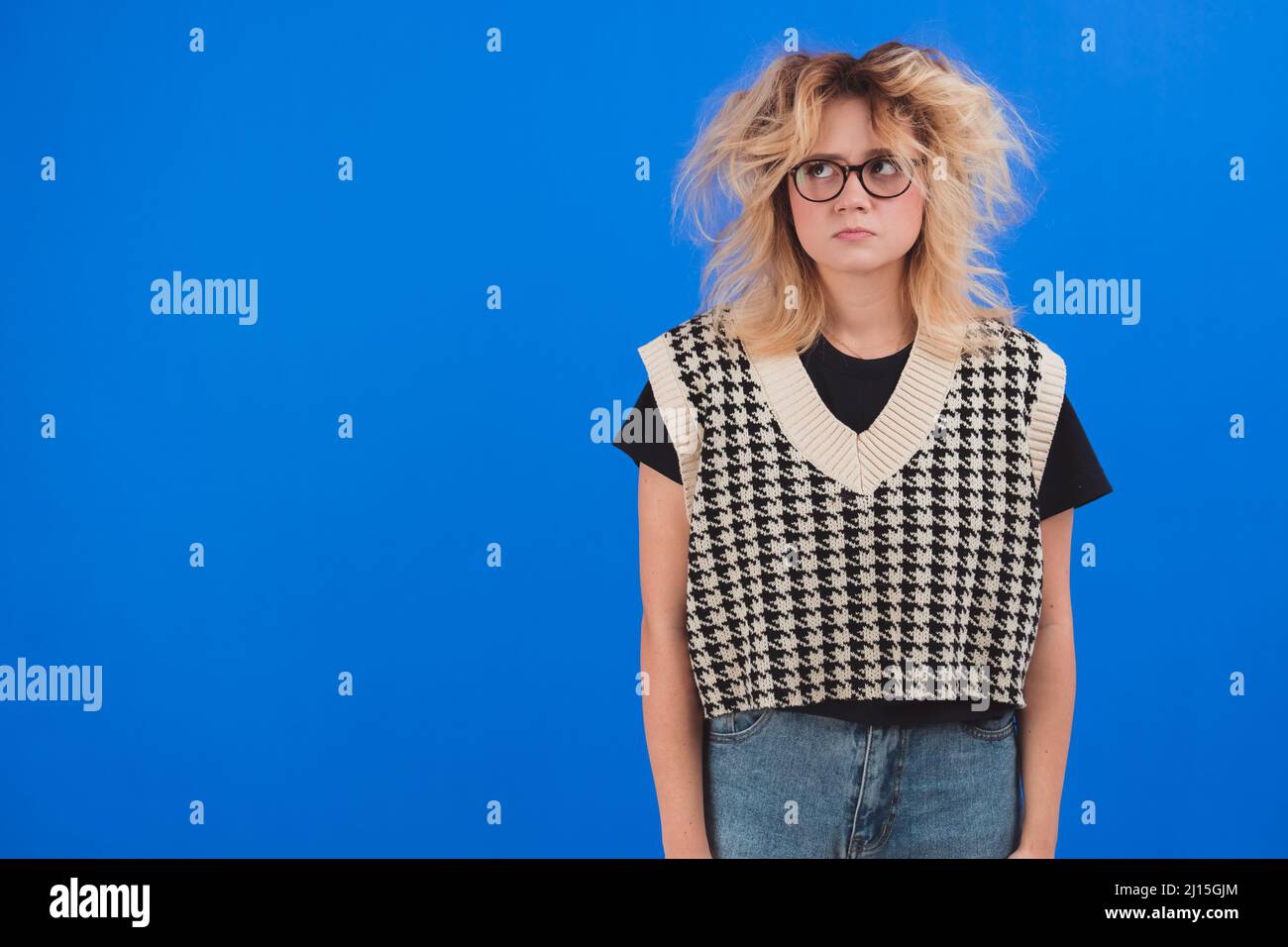 Bouleversé européen adolescente regardant en colère avec des cheveux vieux. Studio tourné sur fond bleu. Photo de haute qualité Banque D'Images