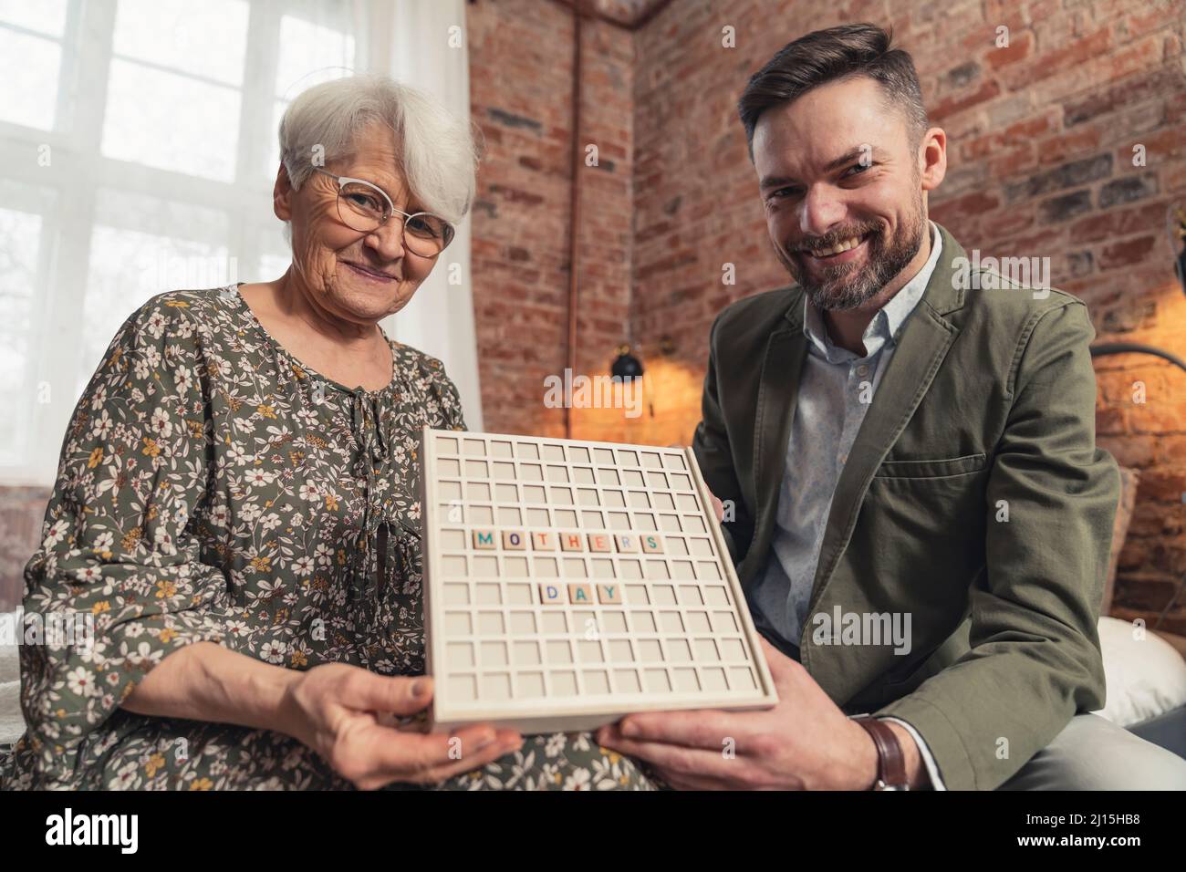 la mère âgée de race blanche et son fils élégant d'âge moyen présentant à la caméra un mot-clé avec une légende Fête des mères . Photo de haute qualité Banque D'Images