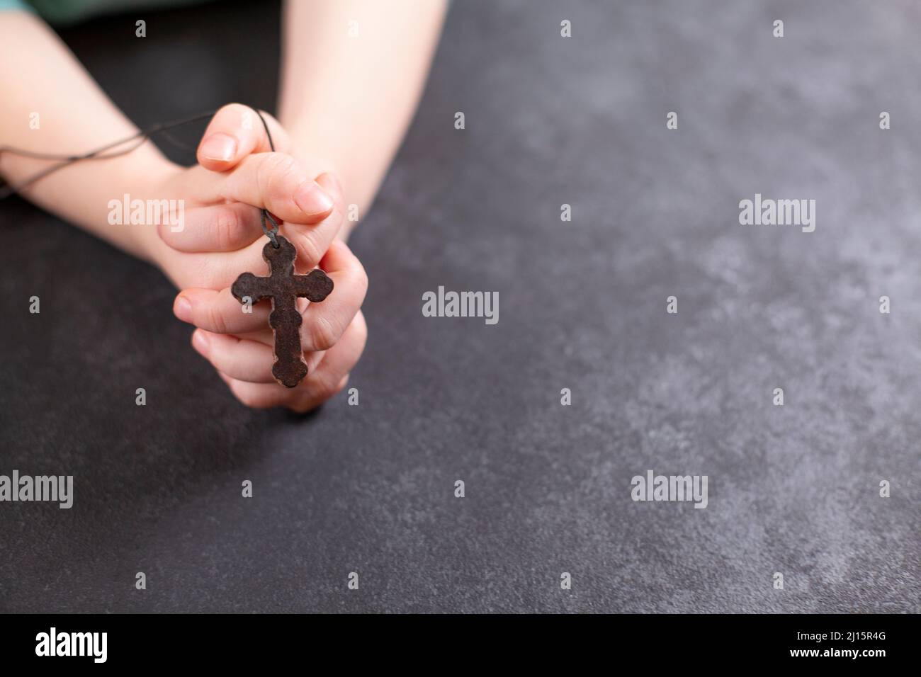Les mains de l'enfant ont classé dans la prière et ont tenu la croix en bois sur fond sombre. Copier l'espace Banque D'Images