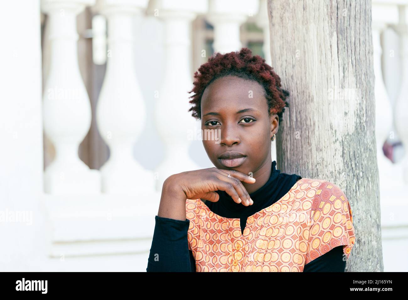 Portrait d'une sérieuse beauté africaine adolescente avec une coiffure moderne, son menton reposant sur sa main, regardant directement dans l'appareil photo; symbole de beauté, Banque D'Images