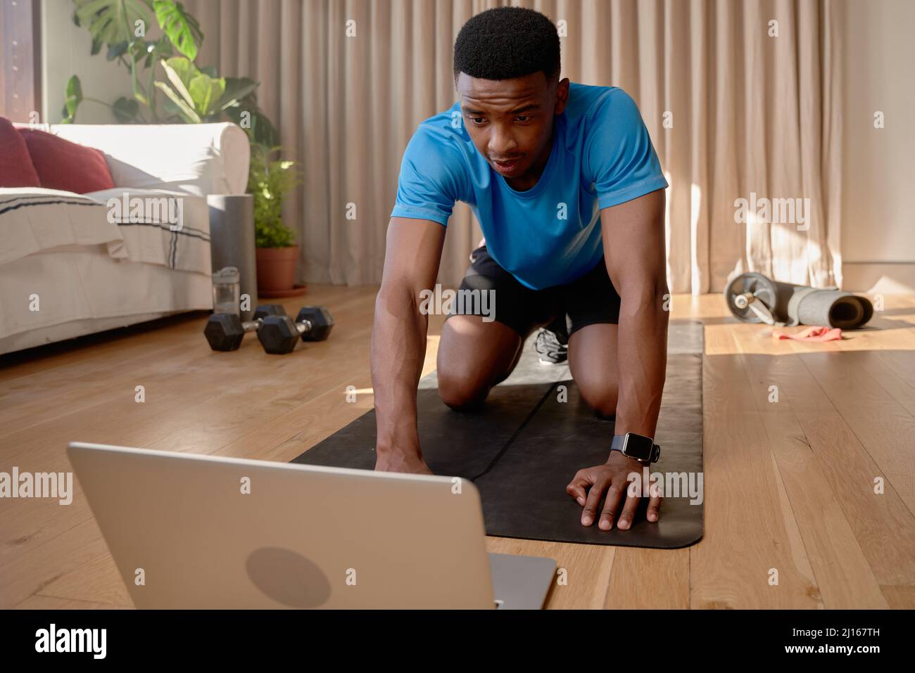 Jeune Afro-américain s'entraînant à la maison sur un tapis en utilisant un ordinateur portable pour assister à un cours en ligne Banque D'Images