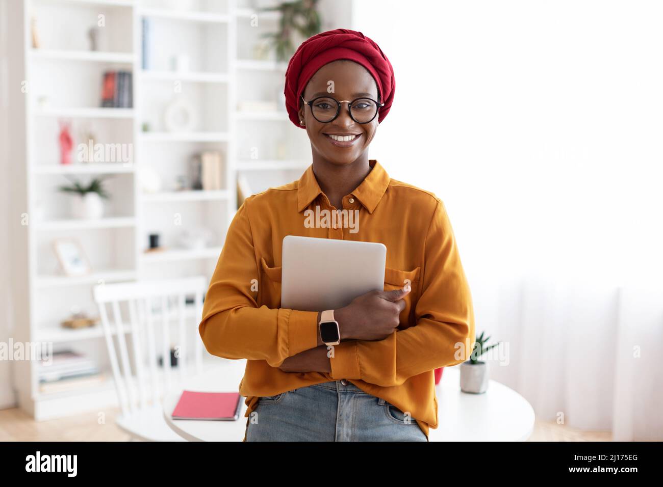 Femme afro-américaine positive posant au bureau, tenant une tablette numérique Banque D'Images