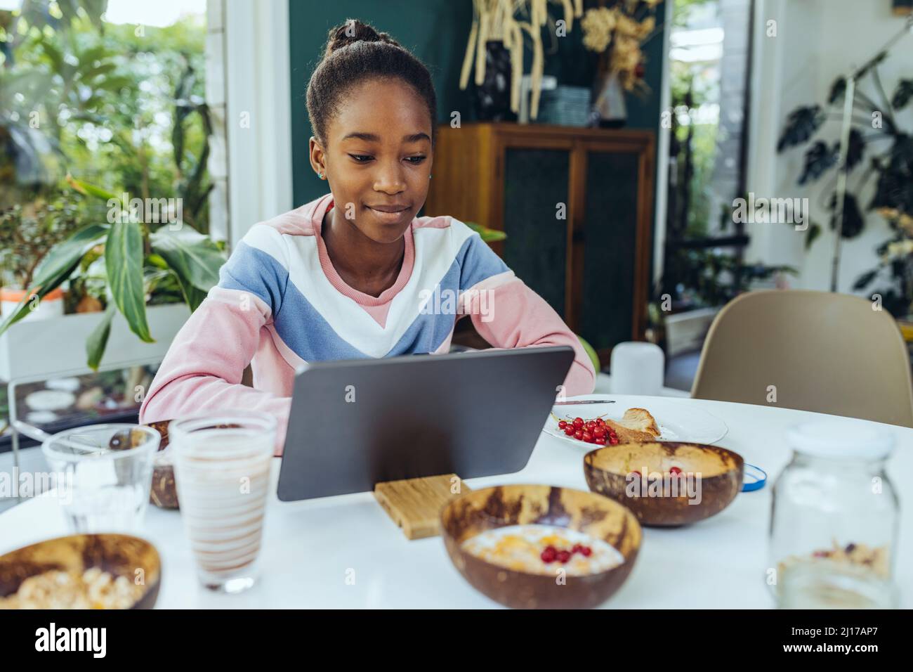 Une petite fille apprenne par le biais d'un PC tablette à la table du petit déjeuner dans la salle à manger Banque D'Images