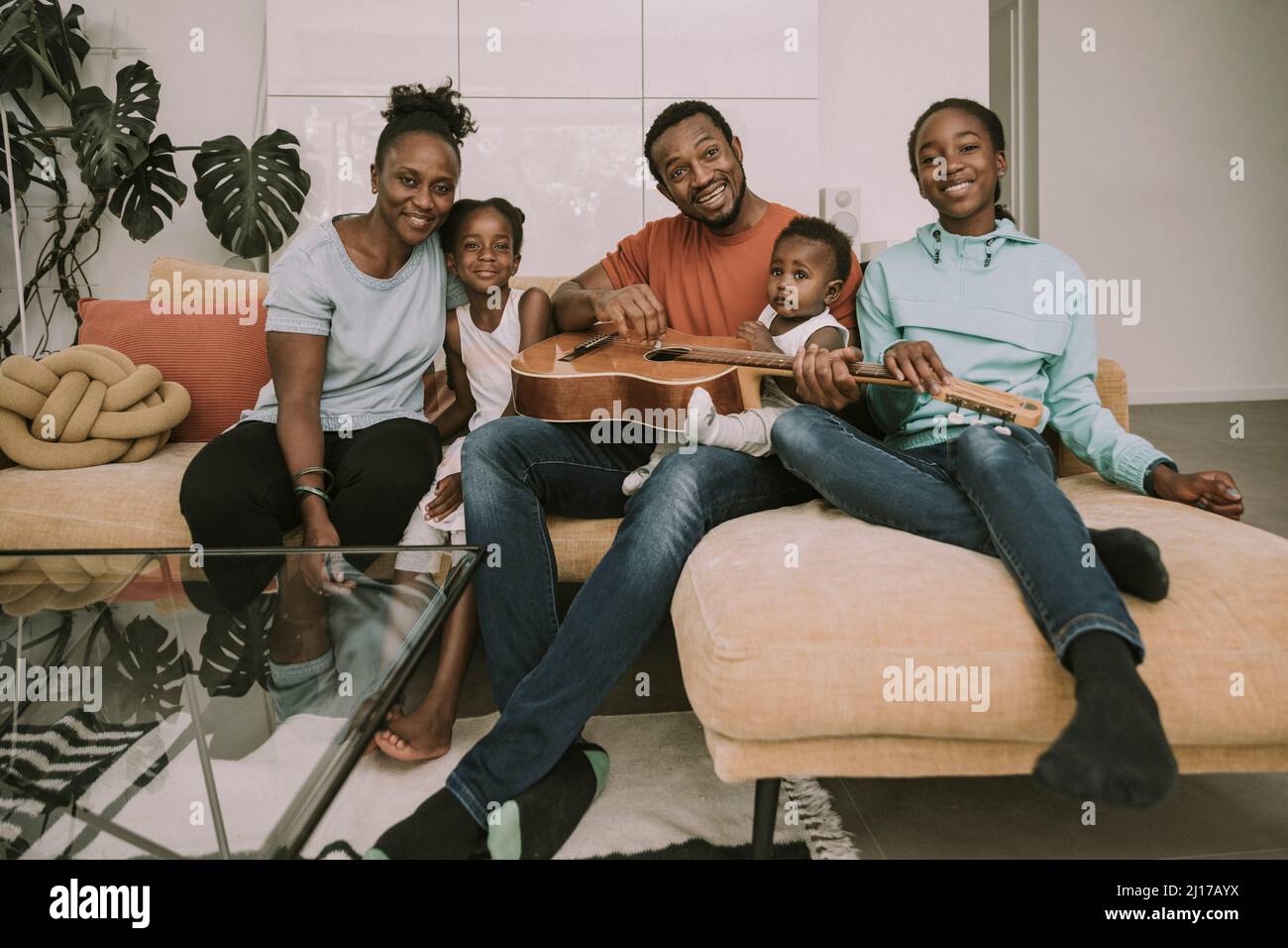Famille souriante avec guitare assis sur un canapé Banque D'Images