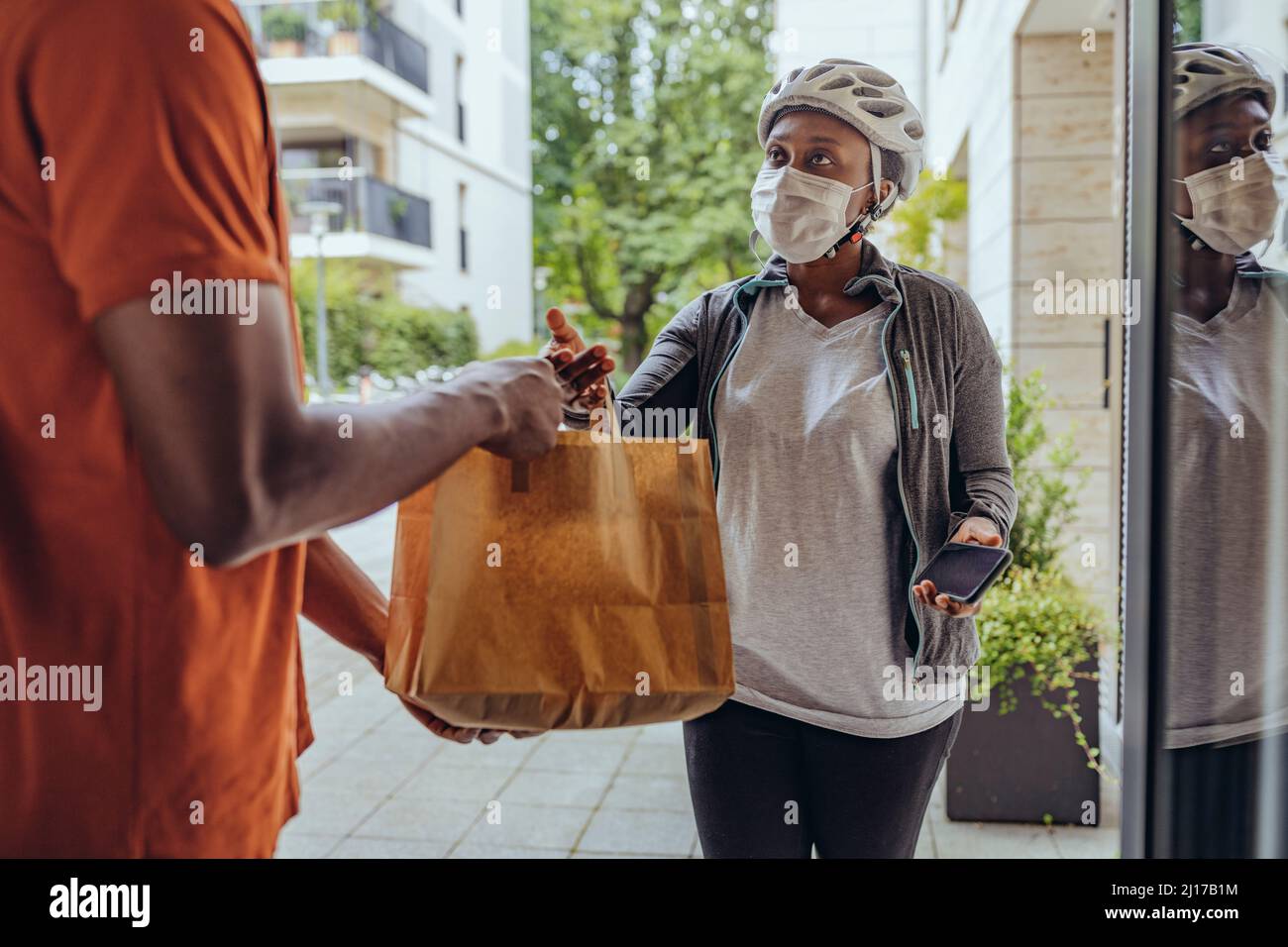 Femme avec masque facial de protection délivrant un sac alimentaire à l'homme à la porte Banque D'Images