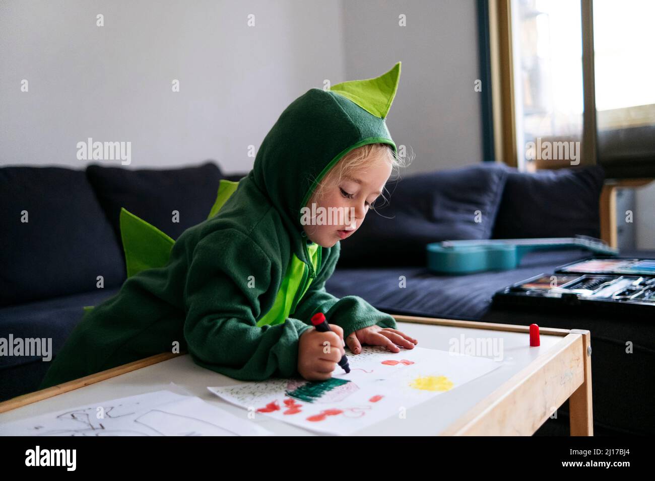 Garçon en costume de dinosaure, dessin sur papier dans la salle de séjour Banque D'Images