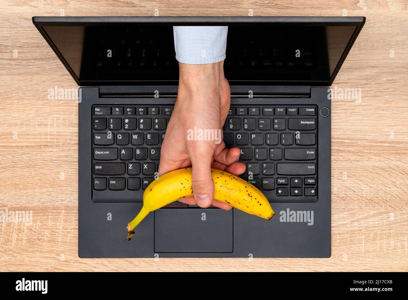 Main de l'homme avec une banane qui se fait sortir de l'écran d'ordinateur. Concept: bureau et alimentation saine Banque D'Images