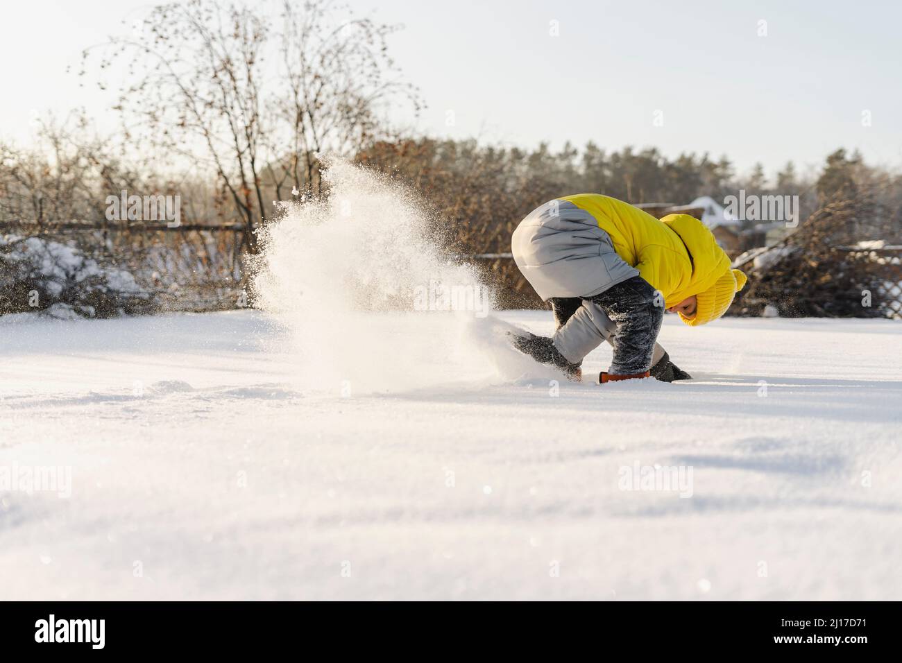Un garçon espiègle qui creuse de la neige dans le jardin en hiver Banque D'Images