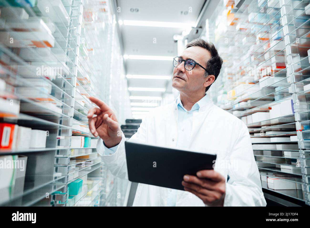 Pharmacien avec un PC tablette pour vérifier les médicaments sur le rack et faire les stocks dans la salle de stockage Banque D'Images