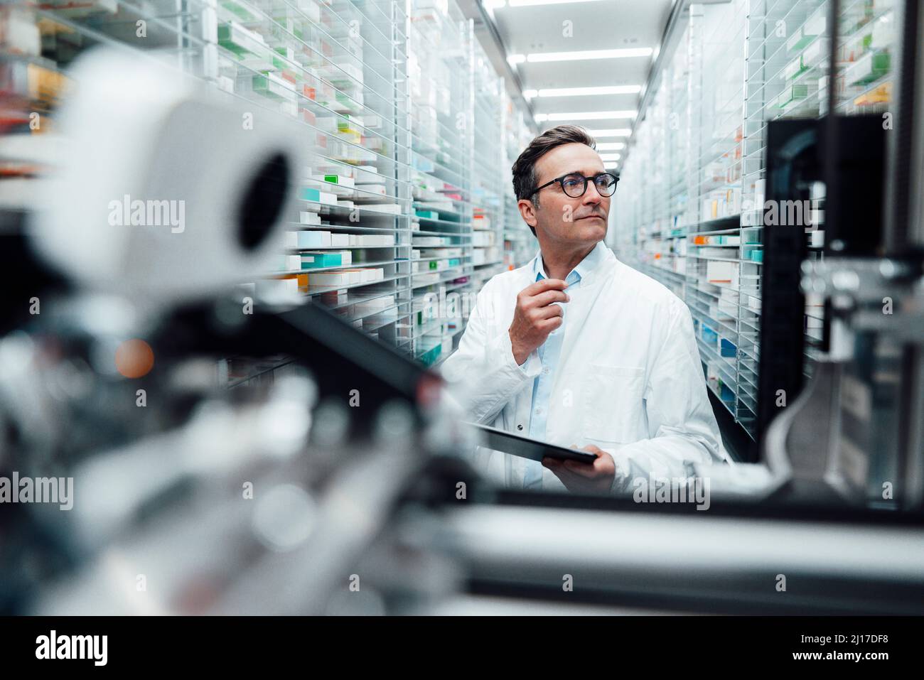 Pharmacien avec un PC tablette vérifiant les médicaments sur le rack et prenant les stocks dans la salle de stockage Banque D'Images