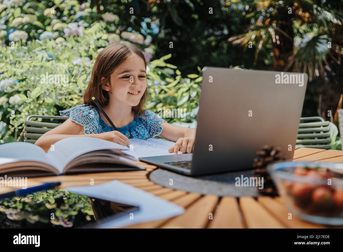 Une jeune fille souriante apprend en ligne par ordinateur portable dans la cour arrière Banque D'Images