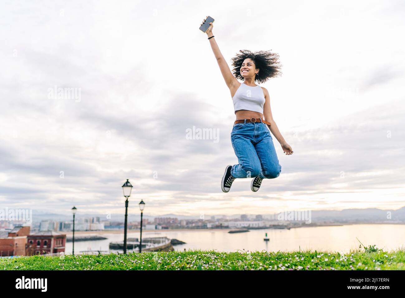 Jeune femme joyeuse avec le saut de téléphone intelligent dans la nature Banque D'Images Jeune femme joyeuse avec le saut de téléphone intelligent dans la nature Banque D'Images