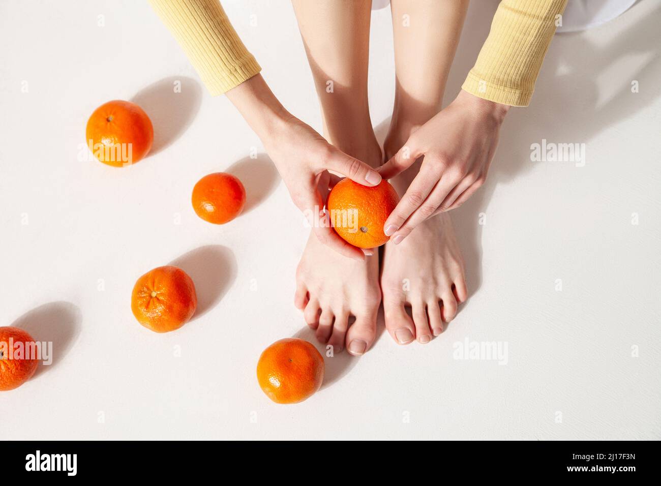 Femme tenant la mandarine au-dessus du pied assis sur le sol au studio Banque D'Images