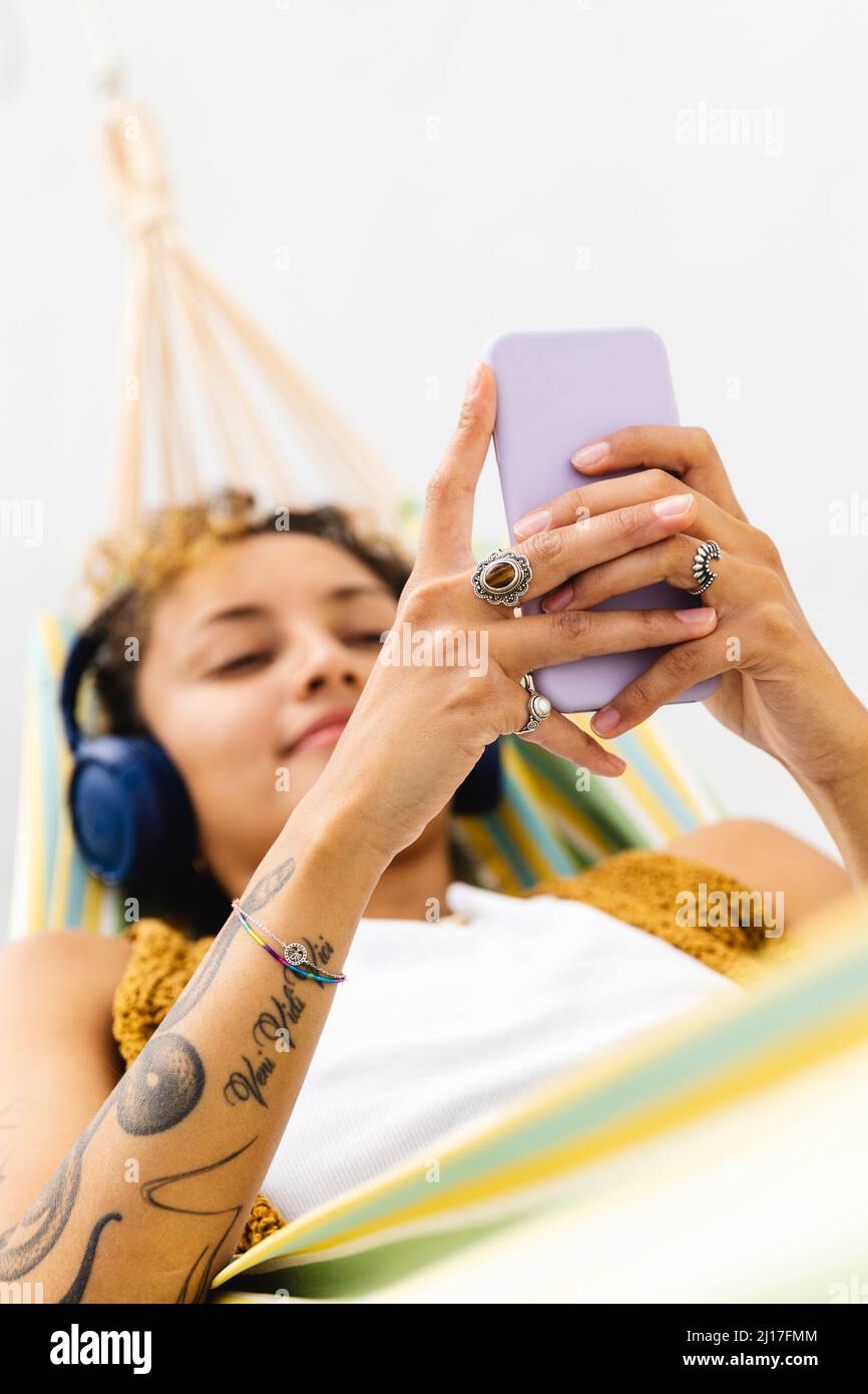 Femme avec tatouage sur le bras en utilisant le smartphone sur hamac Banque D'Images