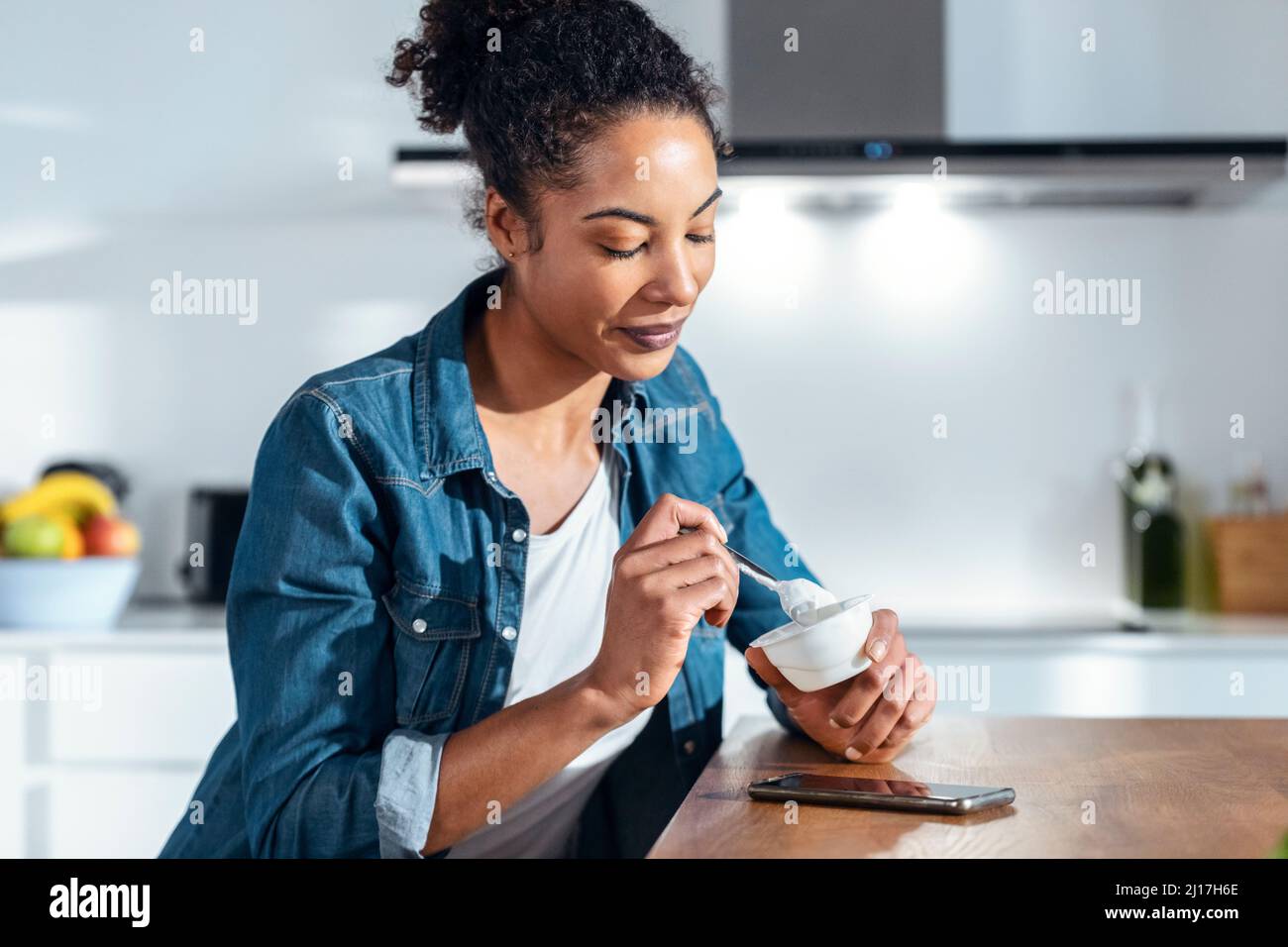 Femme mangeant du yaourt assis dans la cuisine à la maison Banque D'Images