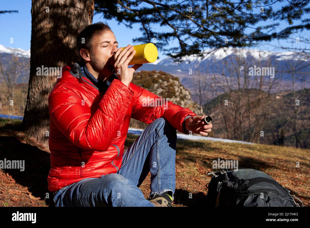 Homme buvant de l'eau à partir d'une bouteille placée sous l'arbre le jour ensoleillé Banque D'Images
