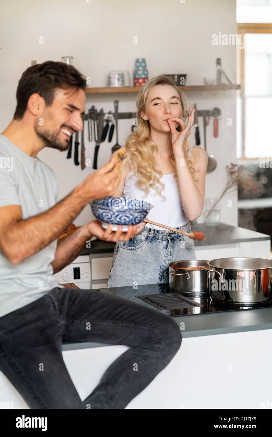 Femme gestante signe ok et regardant le petit ami mangeant spaghetti dans la cuisine Banque D'Images