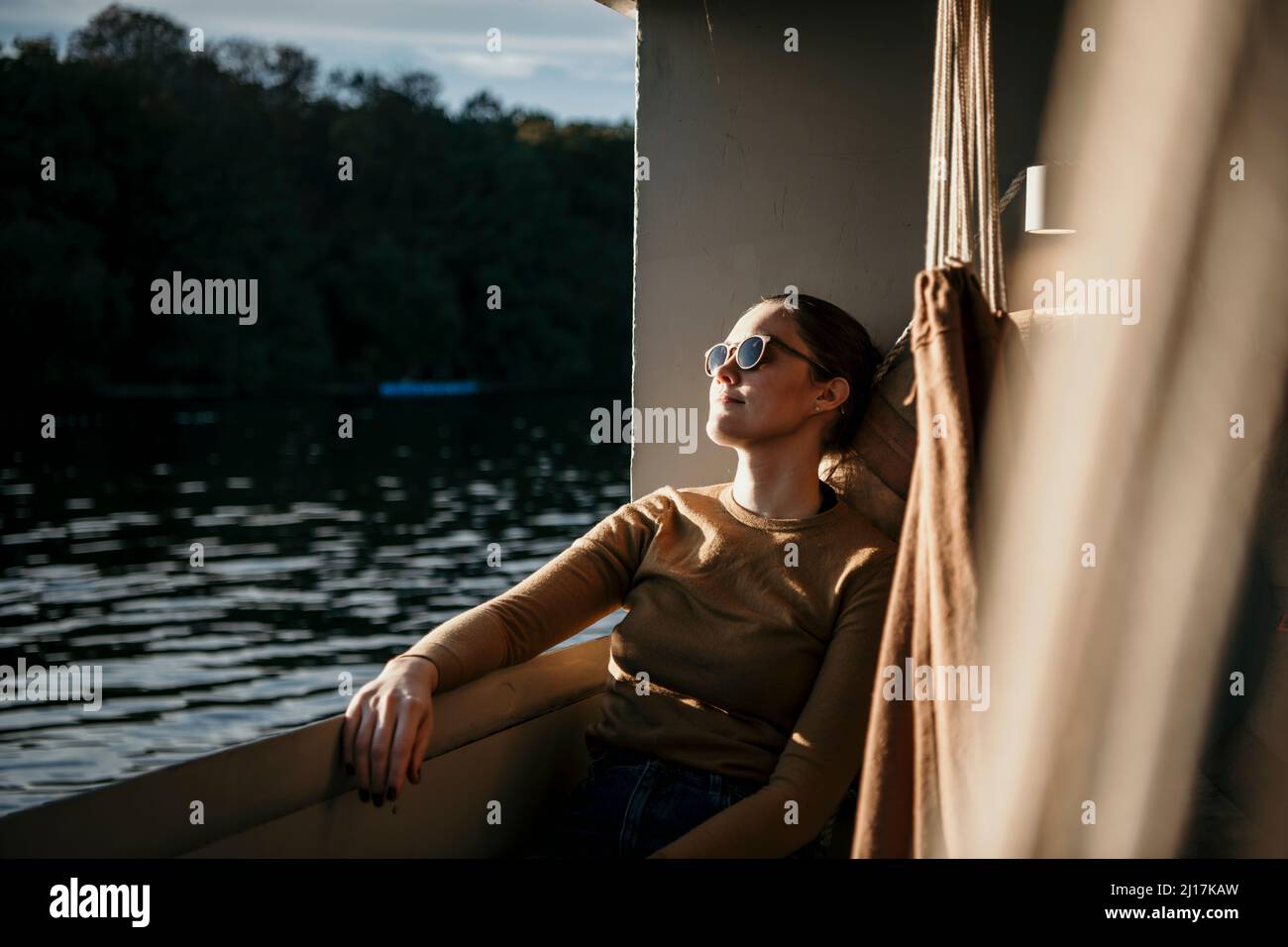 Femme portant des lunettes de soleil assis sur la plate-forme du bateau Banque D'Images